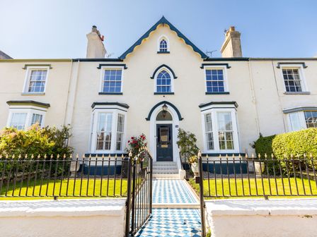The exterior of a white house with blue trim a tiled pathway a black iron gate and green lawn at Abbey Lodge in Llandudno