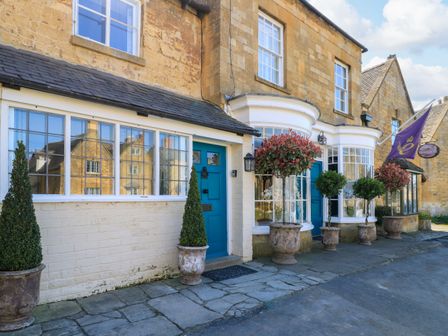 Exterior of a stone building with blue doors and potted plants along the sidewalk at Broadway Cottage in Broadway