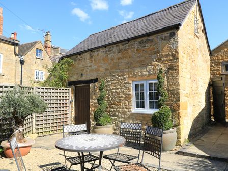An outdoor patio area with a round mosaic table and metal chairs beside a stone building with a wooden door at The Bolt Hole in Broadway