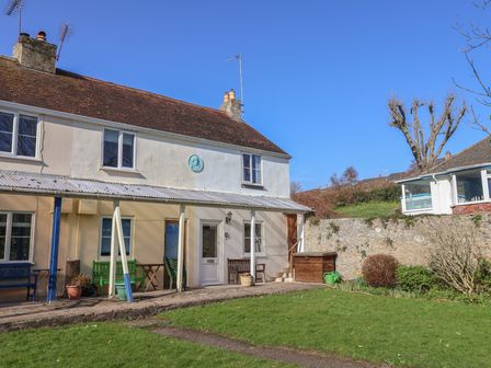 Exterior view of a two-story house with a tiled roof and covered patio with benches and garden at 4 Lymbrook Cottages Lyme Regis