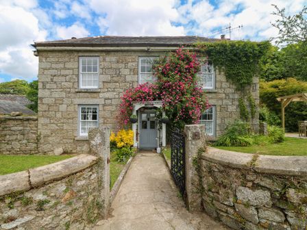 A stone cottage with climbing pink flowers around the doorway and a garden gate at Connies Cottage in Nancegollan nr Porthleven