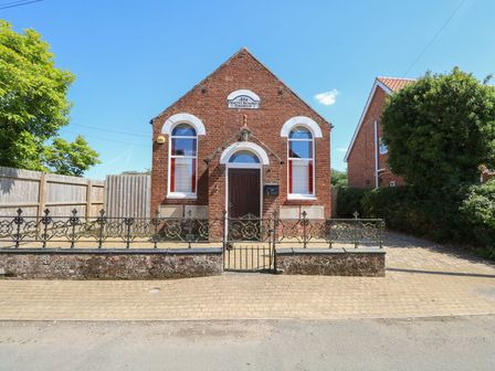A red brick building with arched windows and a wooden door with a small fence in front at The Old Chapel in Foxley near Bawdeswell