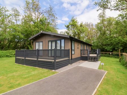 A single story wooden house with a fenced patio surrounded by grass and trees at 18 Manleigh Park in Combe Martin