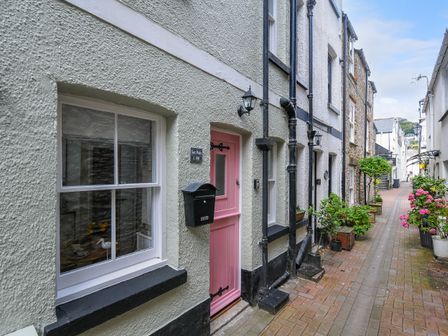 A narrow street with white textured buildings a pink door plants outside at Sea Pinks in Looe