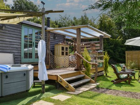 A wooden deck with a hot tub and a white bathrobe hanging outside a cabin at Burr 2 Shepherds Hut in Swimbridge near Barnstaple