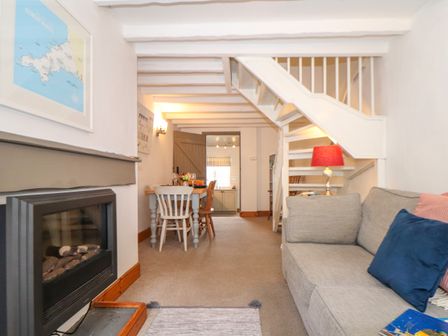 A living room with a fireplace a dining table under stairs and a sofa with cushions at Cobblestone Cottage in Bude