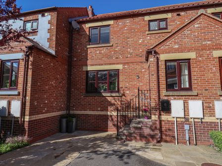 Front entrance of a red brick house with steps flower pot and windows at Esk Side Cottage Ruswarp