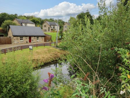A canal with plants in the foreground and stone houses with slate roofs in the background at Canal Cottage in Drumshanbo County Leitrim