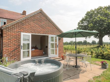 An outdoor patio with a hot tub table chairs and umbrella next to a brick house with open doors showing a wooden bed inside at Orchard View in Redmary DAbitot near Hartpury