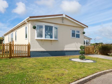A single story house with beige walls and multiple windows surrounded by a lawn and wooden fences at Lowen Lodge in St Merryn near Padstow
