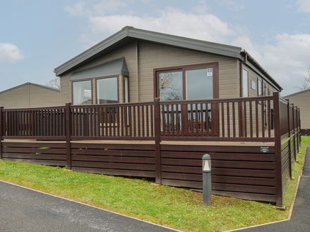 An exterior view of a single-story lodge with a dark wooden fence and a small lawn at Lodge 64 at Riviera Bay Coastal Retreat Brixham