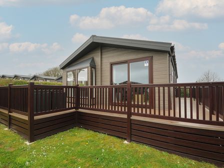 A small house with wooden deck and railing on a grassy area at Lodge 73 at Riviera Bay Coastal Retreat in Brixham