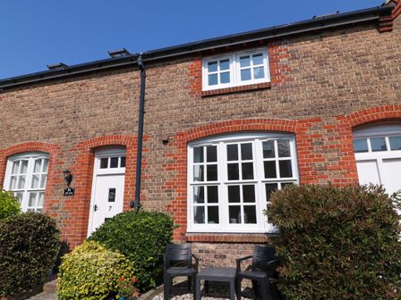 Front exterior of a brick house with white-framed windows and door and garden shrubs with black chairs and table outside at Splash in Weymouth