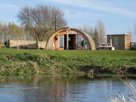 A wooden glamping pod with open double doors near a pond with a picnic table and a barbecue grill outside at Glamping Pod 4 Truce in Lebberston