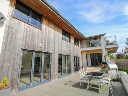 An outdoor patio area with metal table and chairs and a wood oven next to a two story building with wood paneling at Timberdyne Brimfield near Woofferton