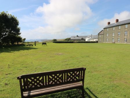A grassy field with wooden benches and houses near the coast at Grassholm View in Solva
