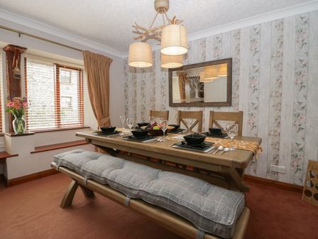 A dining room with a wooden table set for six people wooden chairs and a cushioned bench at 1 Gilpin House Levens
