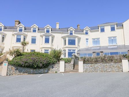 The exterior of a white building with multiple windows and dormers with stone walls and shrubs at Bethan Apartment in Trearddur Bay