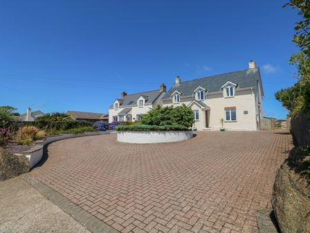 A large house with a paved driveway and greenery under a clear blue sky at Llain Gwynfor in St Davids