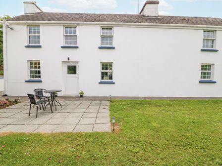 A white house with blue window sills and a small patio with table and two chairs at Aunties in Ballylickey County Cork