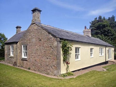 A stone and plaster cottage with multiple windows and chimneys surrounded by grass at The Lake Cottage Near Belford