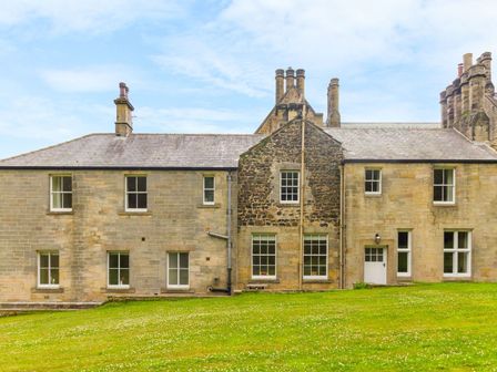 A stone house with multiple chimneys and several windows on a grassy lawn at The Coach House in Belford