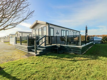 A static caravan with raised deck and outdoor furniture on a grassy plot at Cornerstone near Caernarfon