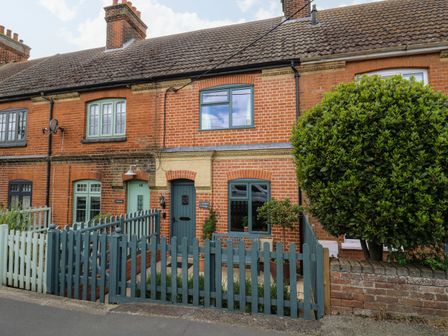 A brick terraced house with blue doors windows and fences and a tree at Compass Cottage in Aldeburgh