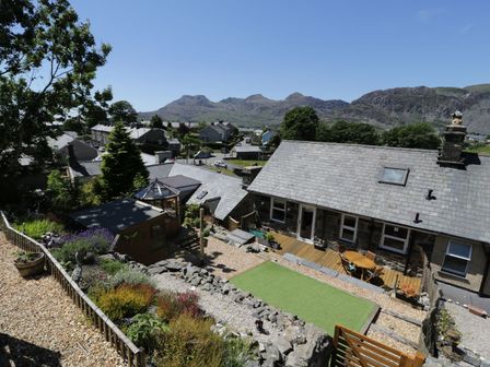 A backyard with a stone house wooden deck table artificial grass garden shed and plants with mountains in the background at Old Post Office in Blaenau Ffestiniog