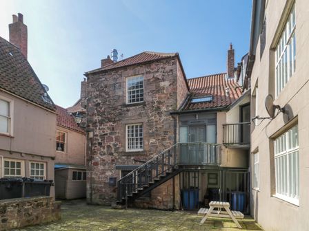 An outdoor courtyard area with stone buildings and an external staircase at The Old Factory House in Berwick-Upon-Tweed