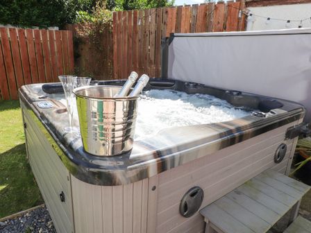An outdoor hot tub with bubbling water two bottles in a metal ice bucket and two champagne flutes on its edge in a fenced garden at The White House in Llanbedrog