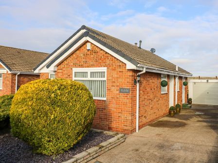 A brick house with a large rounded bush in front and a driveway leading to a garage at Sea Roke in Filey