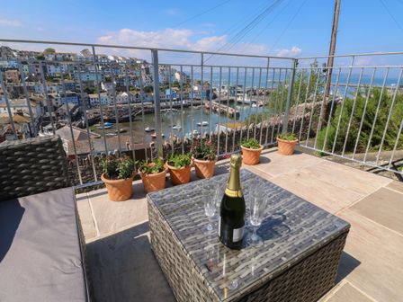 A terrace with a wicker table and sofa with a bottle of champagne and glasses overlooking a harbor with boats at Fishnets in Brixham