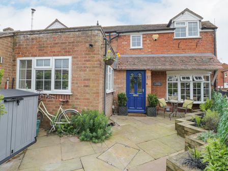 A brick house with a blue door a patio area with two chairs and a table and plants at Jubilee Cottage in Alveston near Tiddington