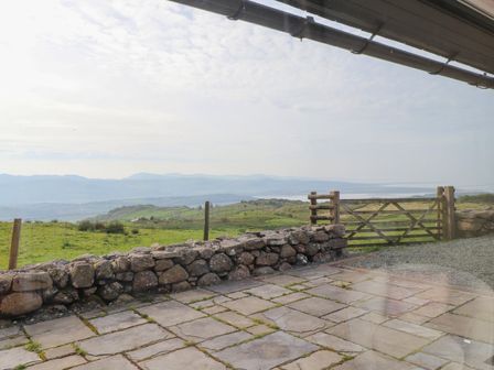A stone patio overlooking a grassy field with a wooden gate and a low stone wall at Beudy Cefn Near Porthmadog
