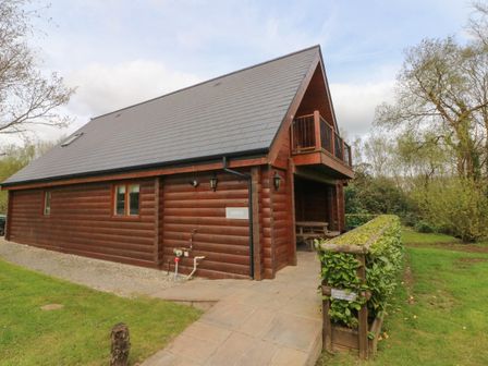 A wooden cabin with a balcony and picnic table surrounded by greenery at Aspen in Dolton