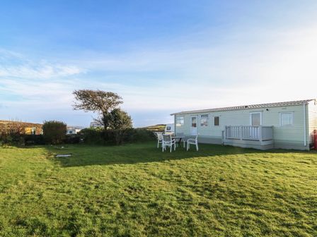 A grassy outdoor area with a caravan a table and chairs near a tree at Tir Glyn Caravan Uwch Mynydd near Aberdaron
