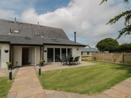 A patio area with a table and chairs outside a house with a slate roof and lawn at Primrose Cottage in Brendon Hill near Roadwater