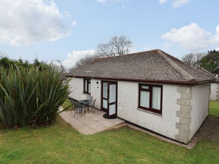 A single story house with a tiled roof and patio furniture outside on a grassy lawn at Kenegie Cottage in Gulval near Penzance