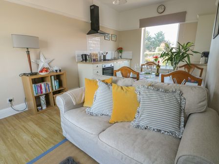 A living room with a sofa and cushions facing a dining table and kitchen at Rhos Retreat No 7 in Rhos On Sea