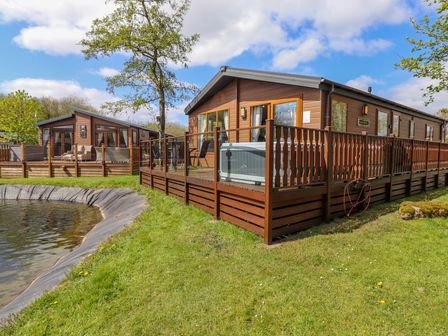 Two wooden lodges with fenced decks near a small pond at Coniston in Carnforth