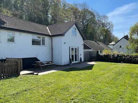 An exterior view of a white house with a tiled roof a grassy yard and a wooden picnic table at The Brambles in Monmouth