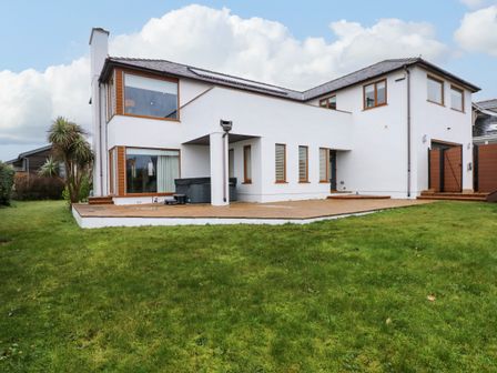 The back view of a two story white house with large windows a patio area and a green lawn at Swyn Llyr in Rhosneigr