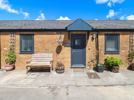 The front exterior of a brick cottage with a blue door two windows a wooden bench and several potted plants at Bluebell Cottage in St Brides-super-Ely near Cardiff