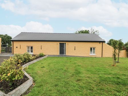 A yellow single story house with a black door and two windows surrounded by grass and small plants at The Farm Cottage in Athy County Kildare