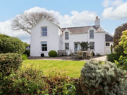 A white house with a garden patio and outdoor furniture surrounded by bushes at Bryn Tirion in Morfa Nefyn