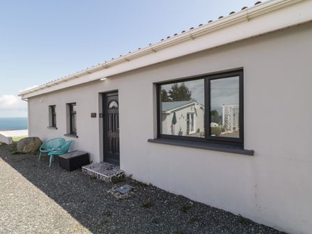 The exterior of a single story building with a black door two small windows two turquoise chairs a black storage box and a gravel ground at Tory Island View in Falcarragh County Donegal