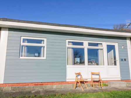 A small house with blue siding two wooden chairs outside and a window at The Sail Loft in Norton Park near Dartmouth