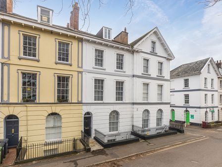 A street view of townhouses with white and yellow facades and black doors at 8 Richmond Road in Exeter
