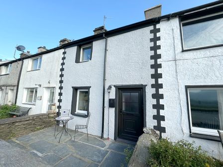 A row of white stucco townhouses with black doors and window frames and a metal table and chairs on a stone patio at Ty Dyffryn in Llan Ffestiniog